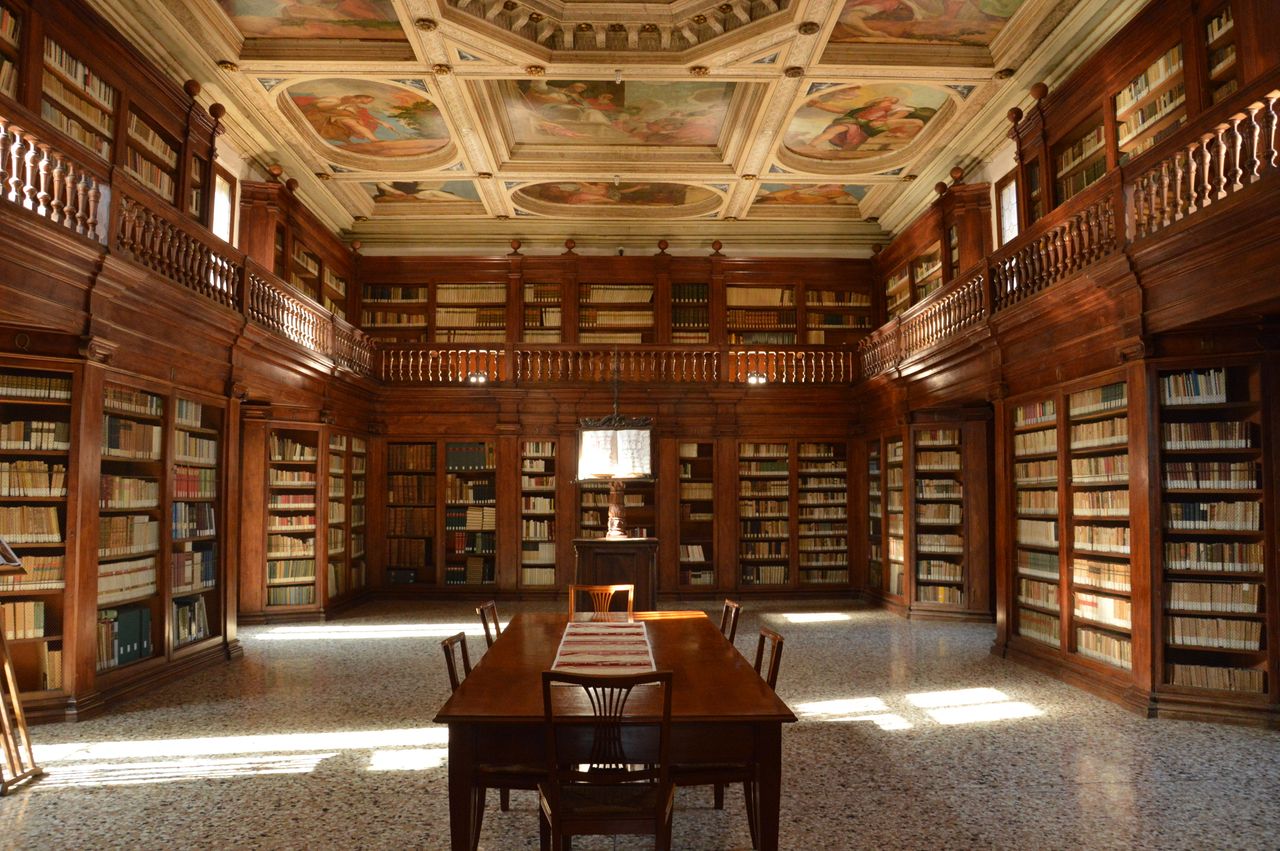 A grand historic library with detailed wooden bookshelves and a beautifully painted ceiling.